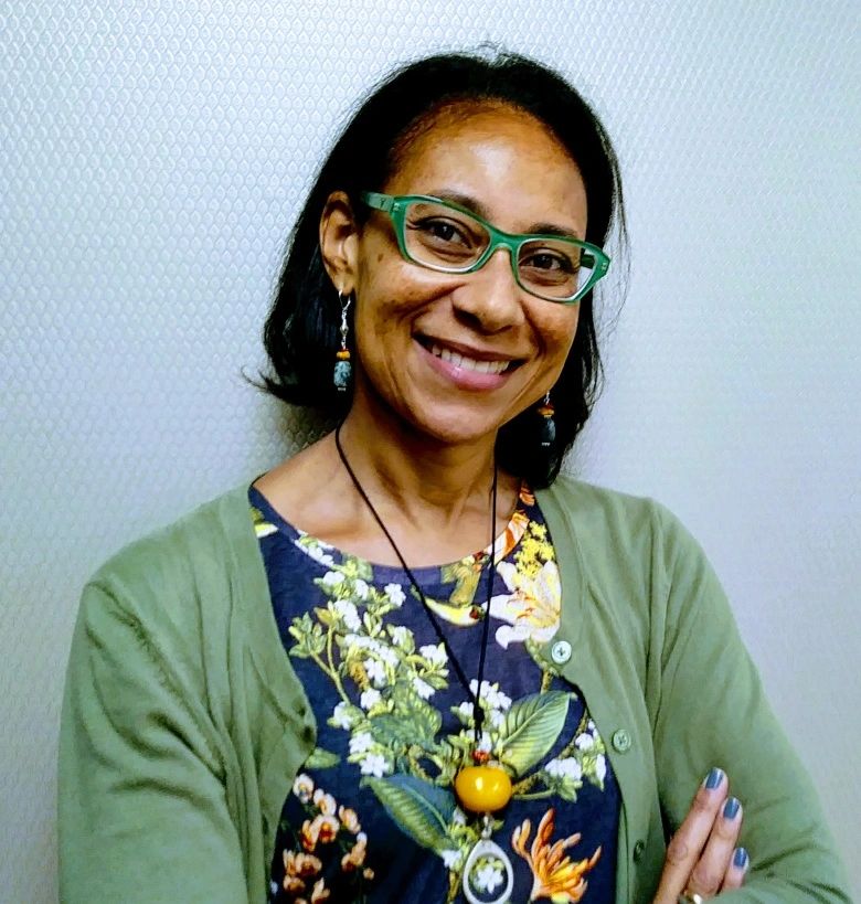 Woman wearing green glasses and a floral dress smiling.
