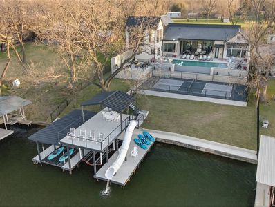 A lakeside house with a dock, slide, and kayaks on the water.