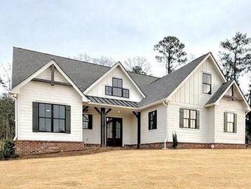 New white house with black windows and brick foundation.