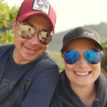 Two smiling people wearing sunglasses and caps outdoors.