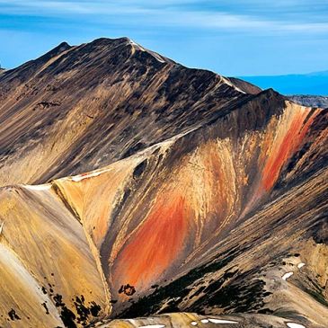 Colorful mountain with red and yellow hues under a clear blue sky.