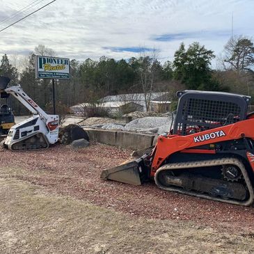 Two compact construction loaders parked on gravel near a rental sign.