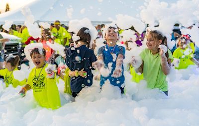Children joyfully playing in a large foam party outdoors.