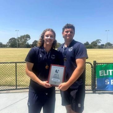 Two athletes proudly holding an award plaque outdoors on a sunny day.