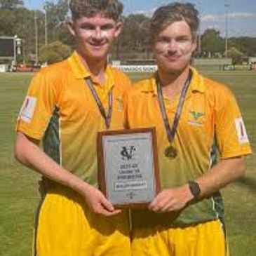Two young cricket players holding a championship plaque and medals.