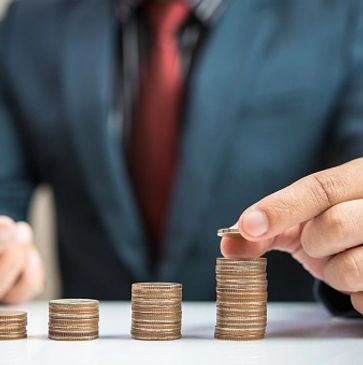 A person stacking coins in ascending order, holding a phone.