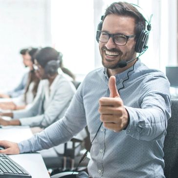 Smiling call center agent giving a thumbs up while working.