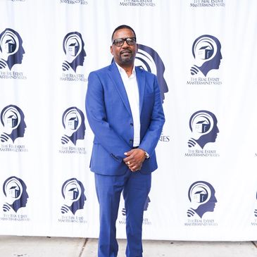 Man in blue suit posing at a real estate event.