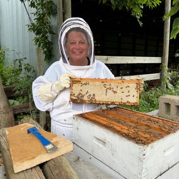 Smiling beekeeper holding a honeycomb frame covered with bees.