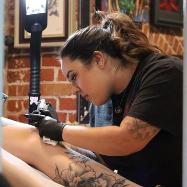 Tattoo artist focused on inking a detailed floral tattoo on a client's leg.