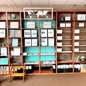 Inviting bookcase with turquoise background, world map, pamphlets, and a Blessed sign.