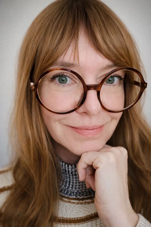 Woman with large round glasses and long brown hair smiling gently.