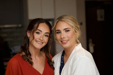 Two smiling women posing indoors, one in red and the other in white.