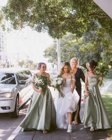 Bride and bridesmaids walking near a limousine with bouquets.
