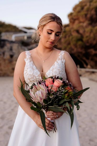Bride in white dress holding a vibrant bouquet on the beach.
