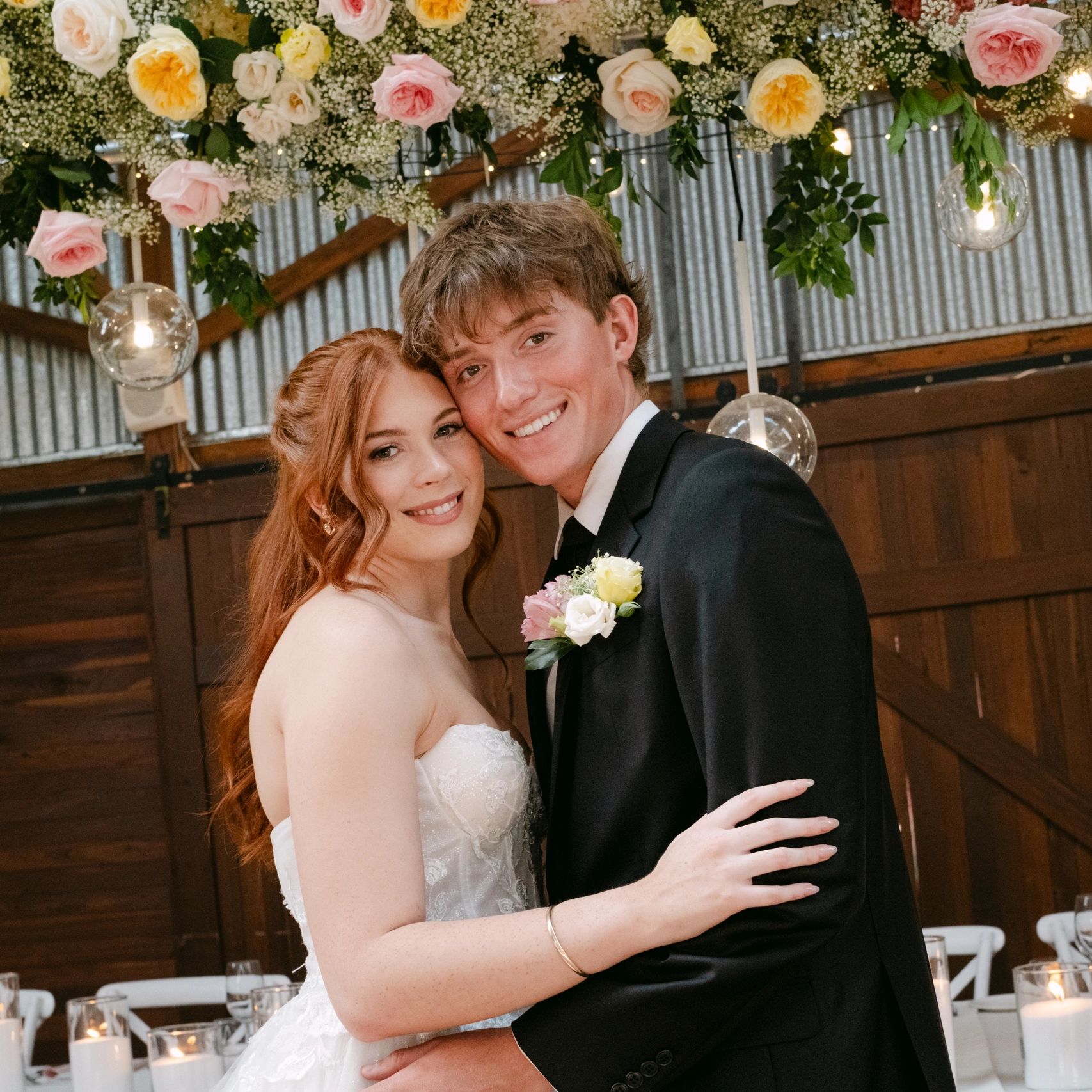 Happy couple in wedding attire embracing under floral decorations.