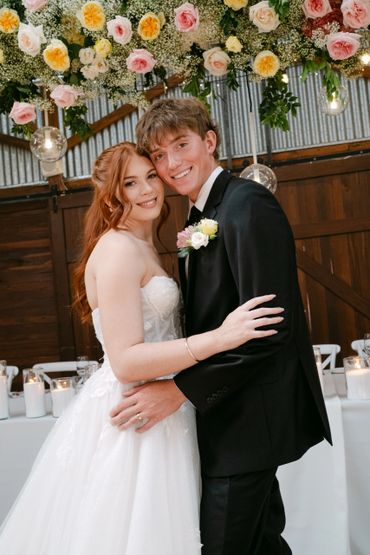 Newlywed couple embracing under floral decorations at their wedding reception.