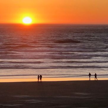 Sunset over the ocean with people on the beach.