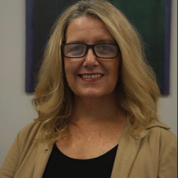 Smiling woman with glasses and blonde hair.