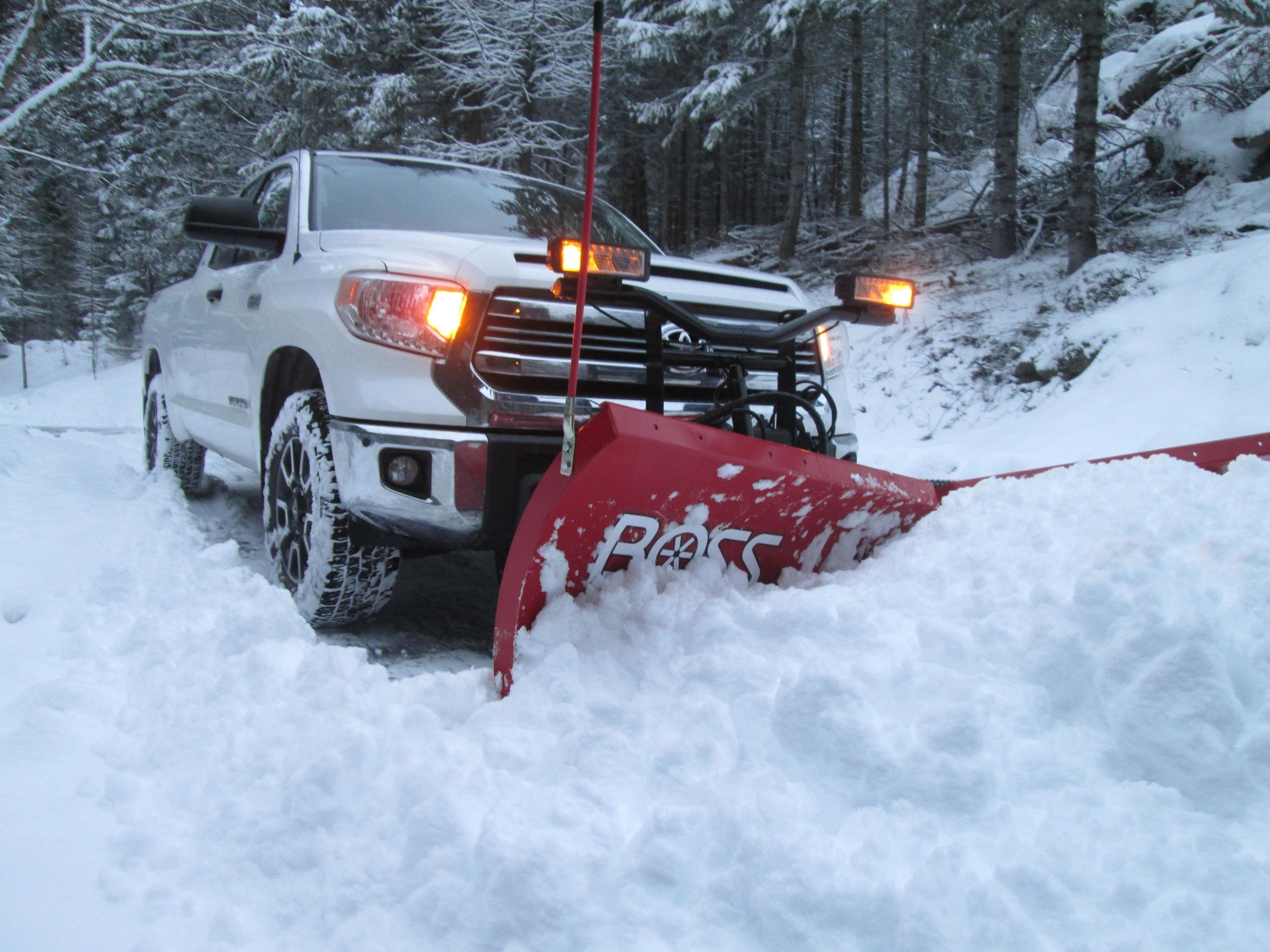 White truck plowing snow with a red BOSS snowplow.