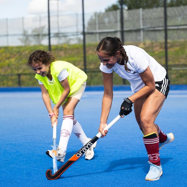 Two girls playing field hockey on a blue turf at Lee Valley Hockey and Tennis Centre in Newham, East London.