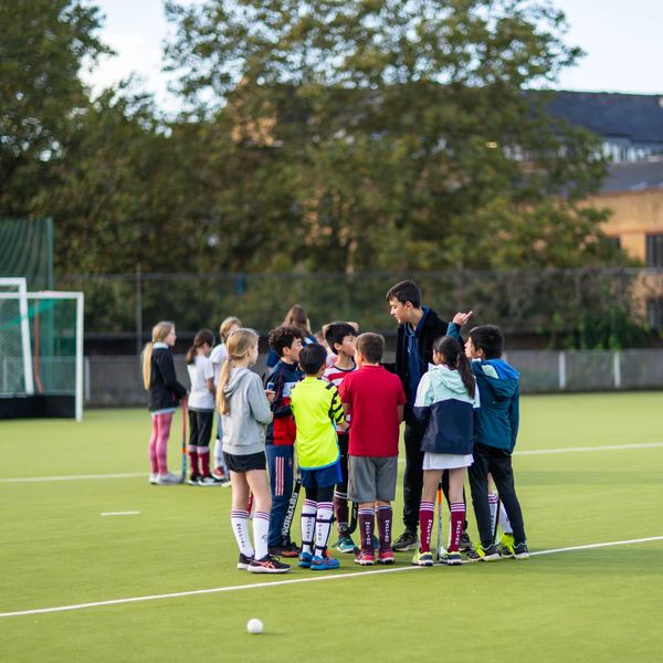 Kids receiving sports instruction on hockey pitch at John Orwell Sports Centre, Wapping, Tower Hamlets, East London.
