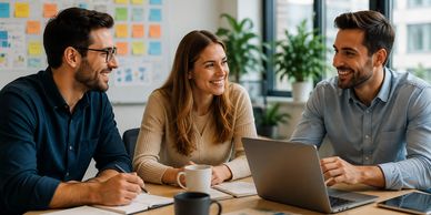 Three colleagues happily discussing work around a laptop in a modern office.