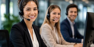 Three customer service agents with headsets smiling at their desks.