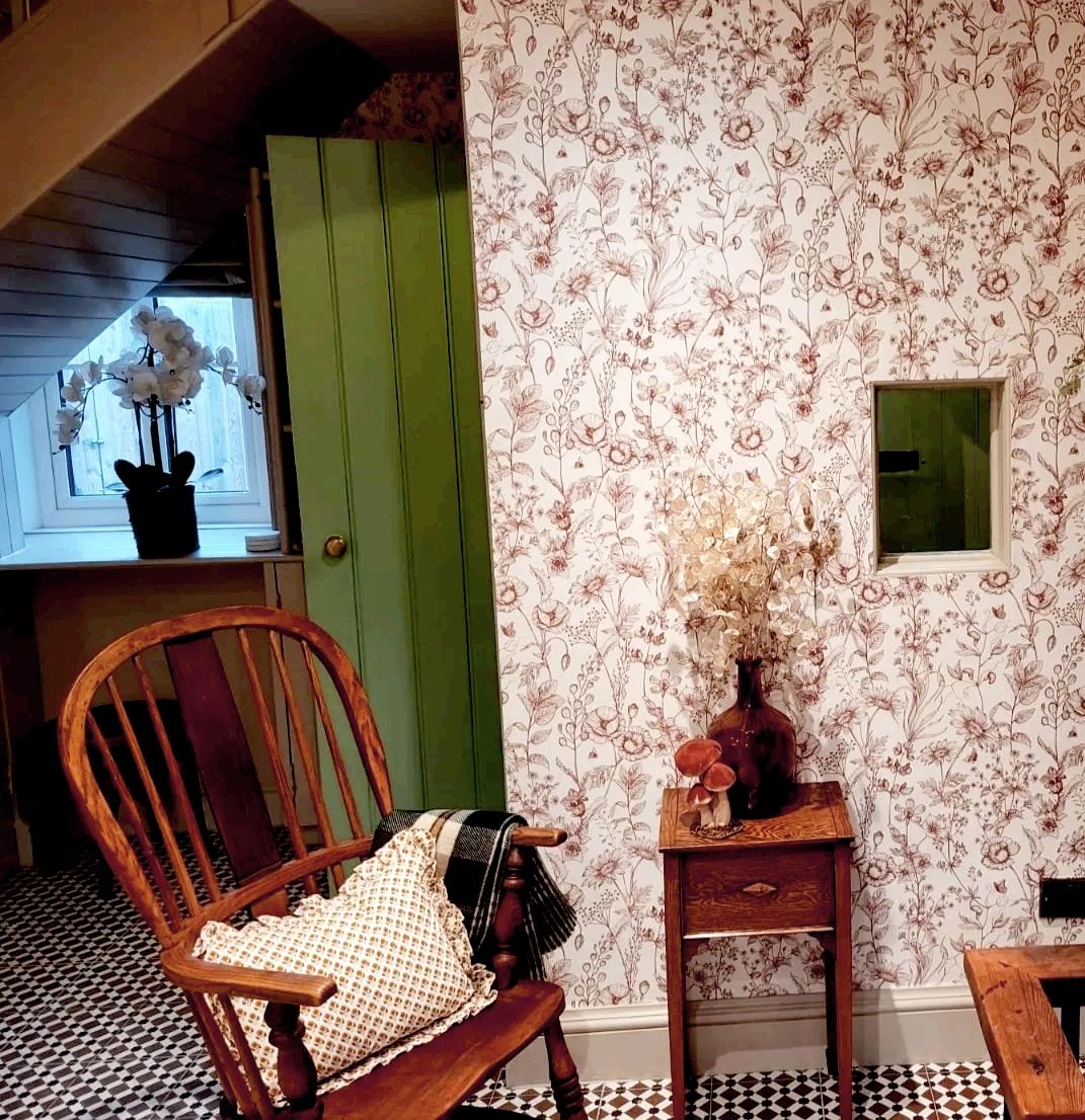 Cozy vintage corner with wooden chair and floral wallpaper.