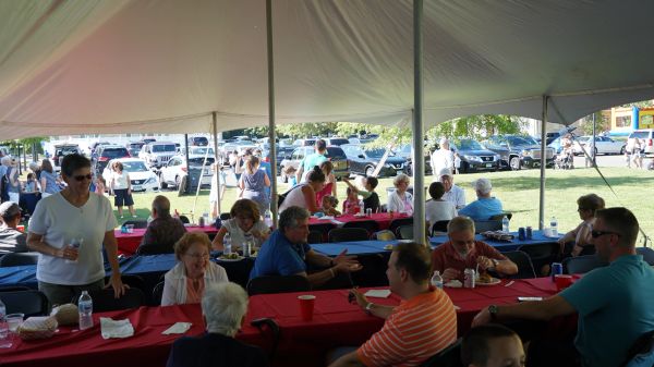 People enjoying a social gathering under a large tent with red tablecloths.