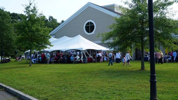 People gathered under a large white tent near a building for an outdoor event.