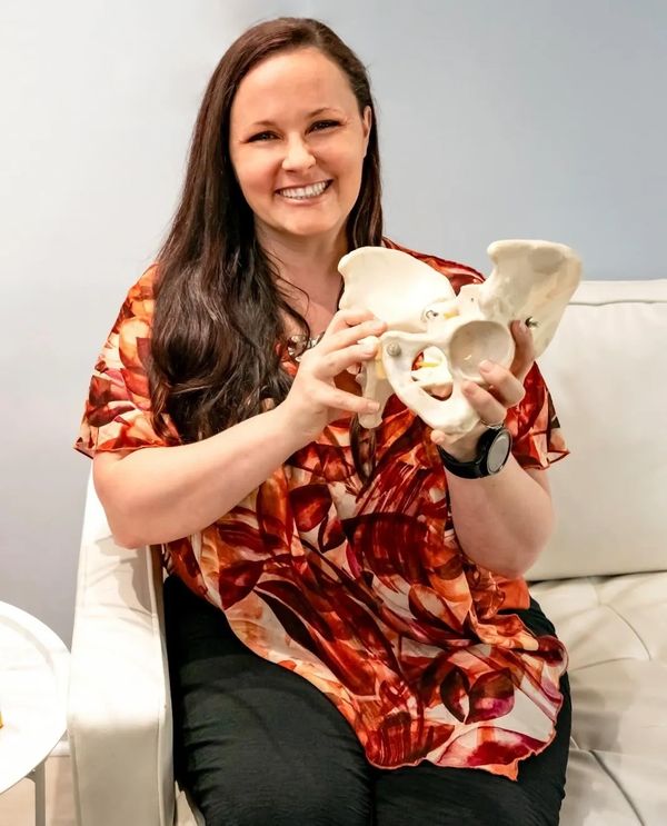 Woman smiling while holding a pelvic bone model.