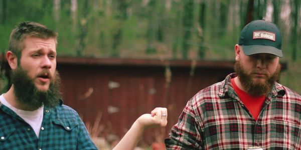 Two bearded men outdoors, one gesturing with a raised hand.