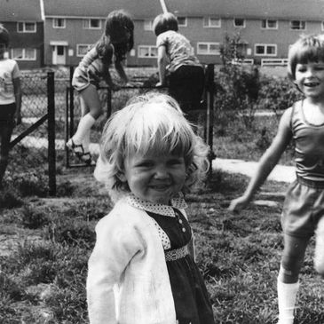 Children playing outside near a fence in a black-and-white photo.