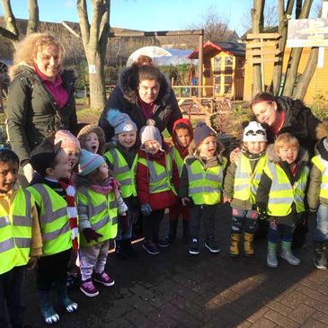 Group of children wearing yellow safety vests with three adults outside on a sunny day.