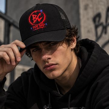 Young man wearing a black cap and hoodie, posing outdoors.