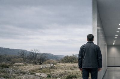Man at edge of lit corridor facing open wild landscape