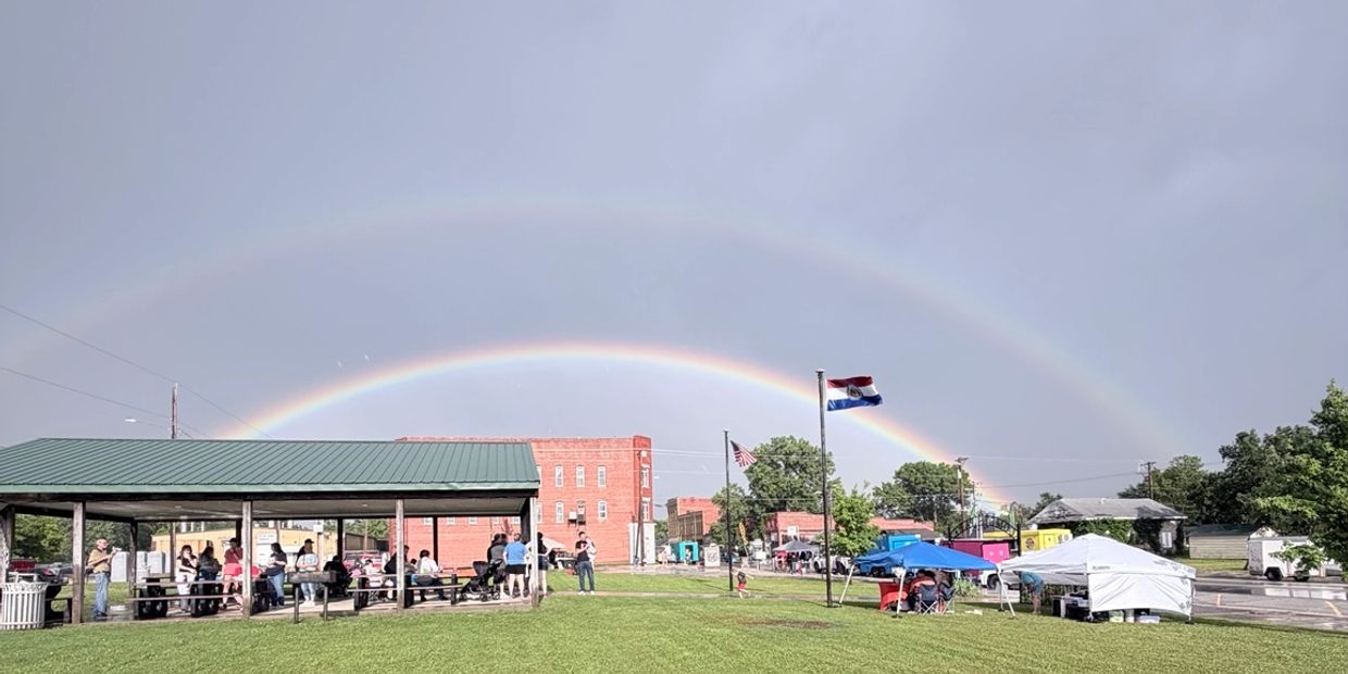 Double rainbow over a park with people gathered under a pavilion and tents.