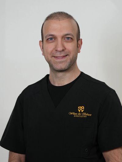 Smiling male dentist in black uniform with dentistry logo.