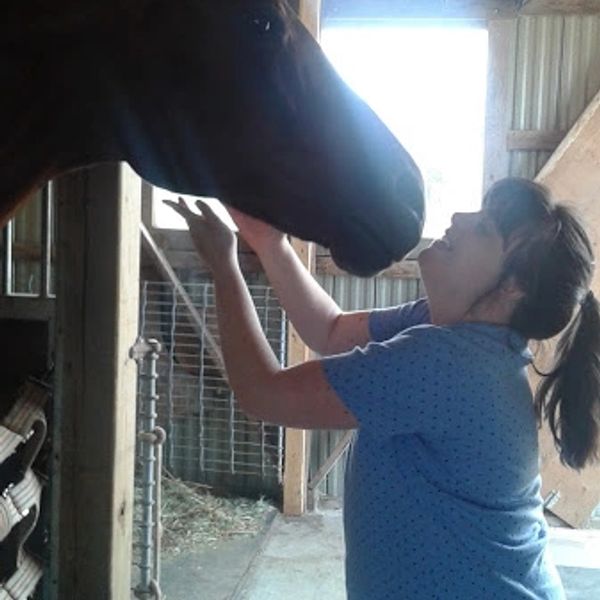 A woman affectionately pets a horse inside a stable.