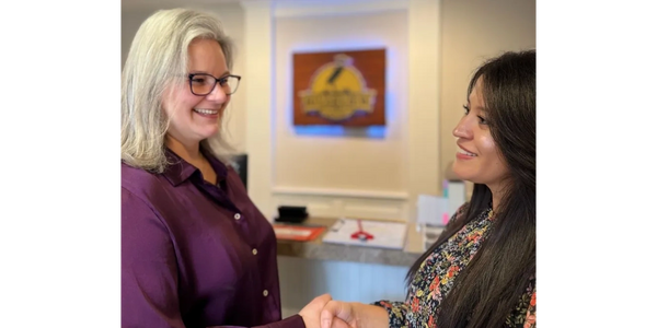 Two women shaking hands and smiling warmly indoors.