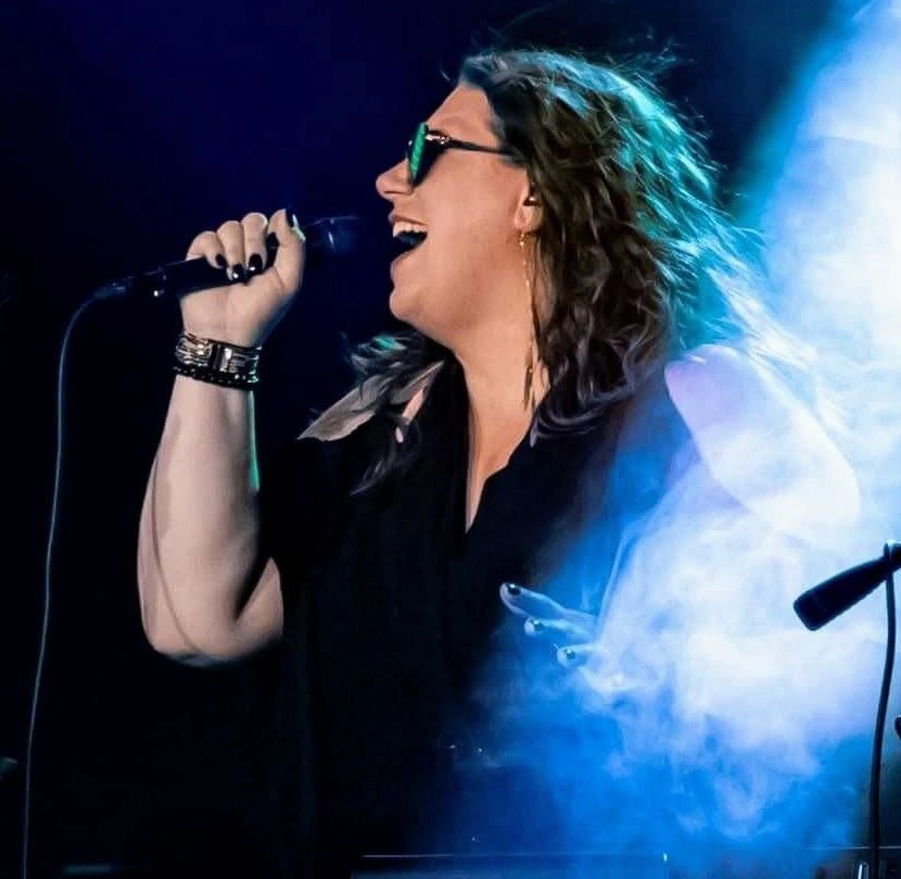 Woman passionately singing on stage with smoke effects.