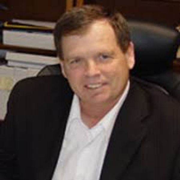 Man in a black blazer and white shirt smiling at the camera.