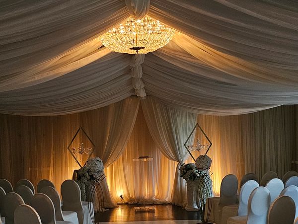 Elegant wedding ceremony setup with draped fabric and chandelier.