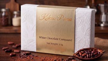 Elegant package of Kokoa Prima white chocolate compound with cocoa beans around.