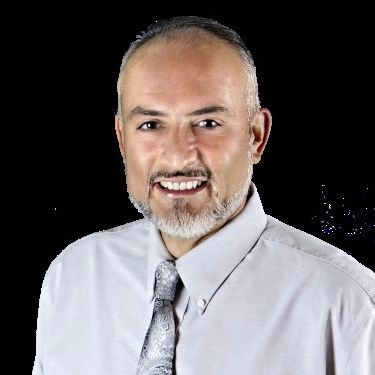 Smiling man in dress shirt and tie against a black background.