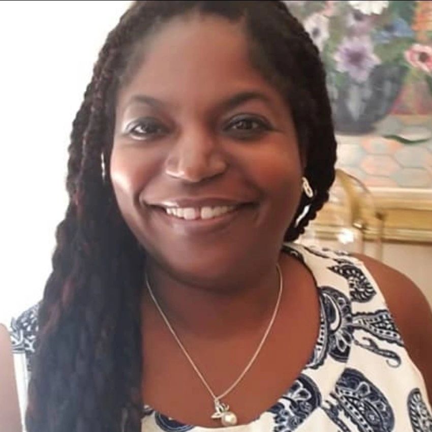 Smiling woman with braided hair in patterned white and blue clothing.