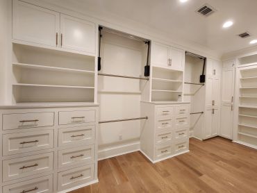 Spacious empty walk-in closet with white shelves and wooden floor.