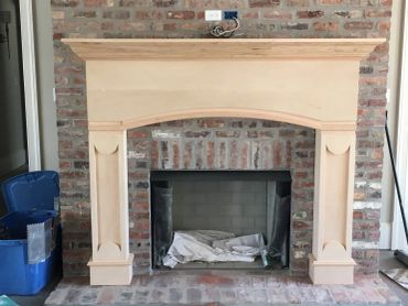 Unfinished wooden fireplace mantel against brick wall.