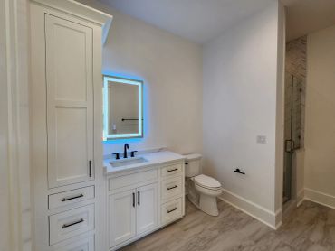Modern bathroom with white cabinetry and illuminated mirror.